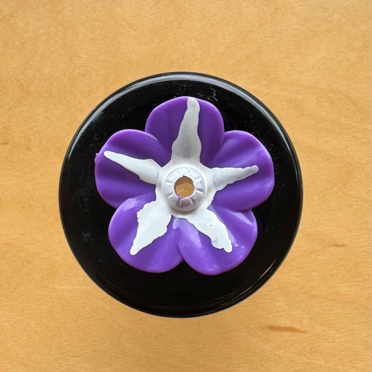 Purple flower-shaped object on a black base against a wooden background