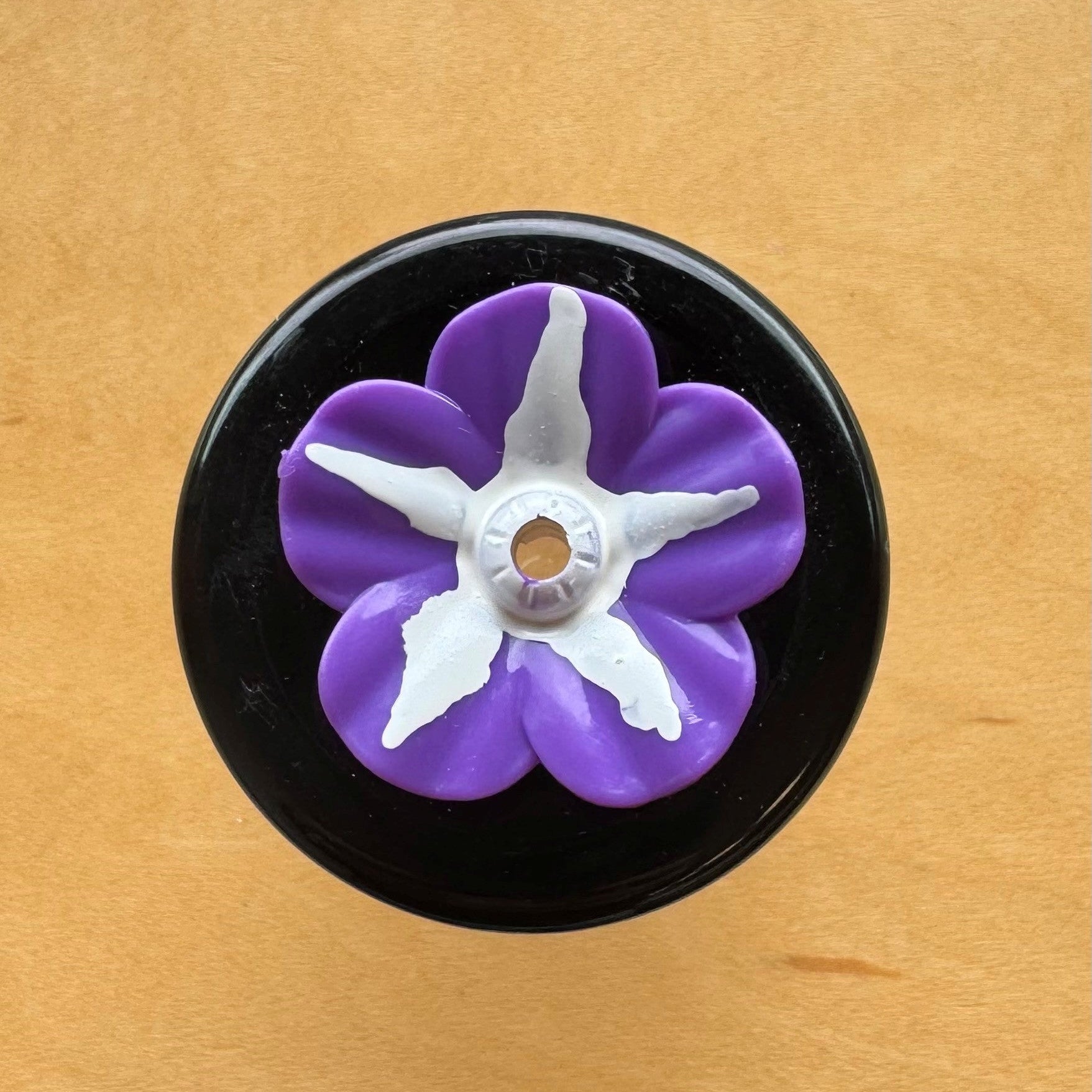 Purple flower-shaped object on a black base against a wooden background